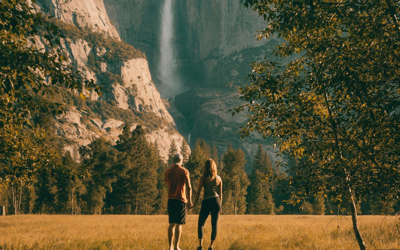couple standing on tree trunk looking at field and forest by Jared Rice courtesy of Unsplash.